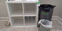 Front view of white 4-cubby shelf with two gray trash cans beside it