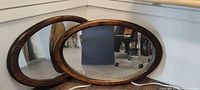 Both oval wood framed mirrors side by side