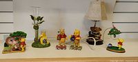 Group shot of lamp base, tulip vase, six Pooh figurines, accent light
