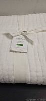 Folded white Pottery Barn pick-stitch quilt with tag and ribbon