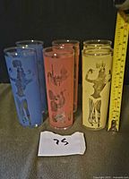 Six coloured Tom Collins glasses shown upright with tape measure for scale