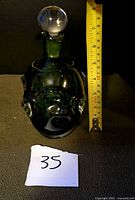 Front view of green art glass decanter with stopper, tape measure shows height ~9 in