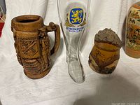 Three drinking vessels: carved wood stein, Lowenbrau glass boot, birch bark stein