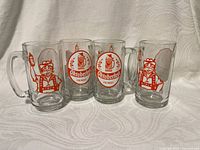 Four clear glass beer mugs showing front graphics