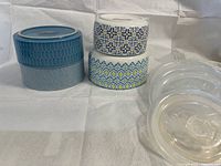 Side view showing two teal containers stacked and two patterned white containers stacked plus two lids