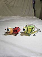 Two painted metal bug decorations on white surface showing side profiles