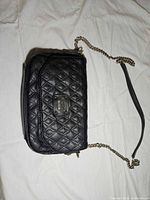 Front view of black quilted Guess purse showing logo plaque and chain strap