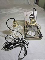 Two gold wire-cage pendant lights, cords and plug visible, one in box