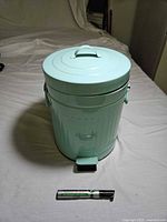 Front view of mint green metal pedal trash can with marker for scale