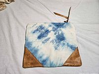 Front view of tie-dye clutch showing canvas body and leather corners