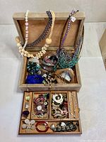 Open jewelry box displaying necklaces draped over lid and assorted jewelry in compartments
