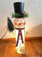 Front view of illuminated glass snowman with top hat, scarf and tree accent