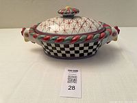 Front view of covered casserole showing chicken head handles, checkered body, lid in place