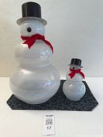 Both glass snowmen side by side on mat showing relative sizes and accessories