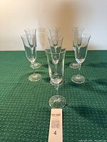 Seven crystal champagne flutes standing on green surface with lot tag visible