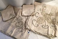 Both folded tablecloth sets with napkins showing embroidery, cutwork and original stickers