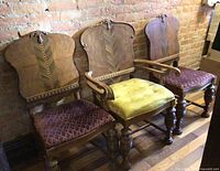 Three vintage chairs aligned against brick wall: two side chairs with burgundy seats, one armchair with mustard seat