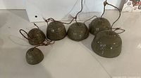 Front view of six olive green ceramic bells lined in size order