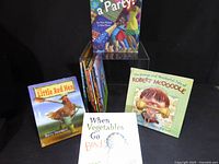 Group of children’s books standing and stacked showing covers of The Little Red Hen, When Vegetables Go Bad!, A Party!, Robert McDoodle plus spines of other titles
