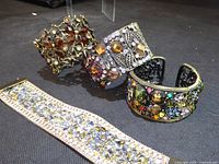 Three ornate cuff bracelets and wide rhinestone stretch bracelet on dark surface