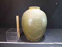 Front view of large green glazed jar with ruler and cube for scale