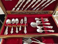 Open wooden chest showing assorted 1847 Rogers Bros silverplate flatware pieces arranged in red velvet slots