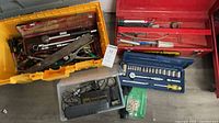 Overview of lot showing yellow tote full of hand tools, red toolbox with tools, blue socket case, clear bin with chargers and hardware