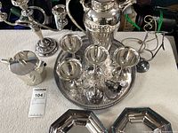 Group shot of all silver-plated items on towel including tray, pitcher, shaker, goblets, plates, candelabrum, wine holder