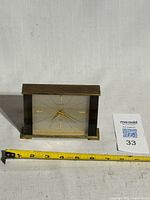 Front view of brass Looping alarm clock with tape measure showing width (≈4 in.)