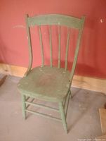 Front-angled view of green wooden chair showing spindle back and seat wear