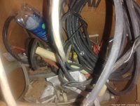 Close-up of box contents showing coiled black cables, white wires, red/black hookup wire, blue bottle, and hardware pieces