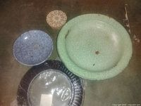 Overhead view of three enamelware pieces: green basin, wrapped dark platter, blue bowl