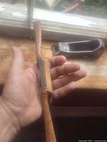 Hand holding wooden drawknife with metal rasp plane in background