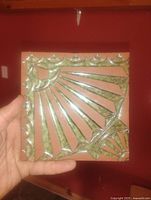 Front view of square red clay tile with green glazed raised sunburst pattern