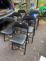 Six black folding chairs arranged on driveway