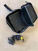Portable DVD player inside open carrying case with screen visible, power adapters beside it