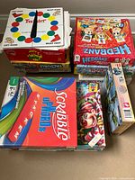 Front view of stacked board games including Twister spinner, Hedbanz, Pictureka!, Scrabble Junior, Candy Land/Chutes and Ladders, Clue, Mille Bornes