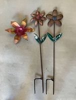 Front view of the three metal flower stakes showing design, colours and ground prongs