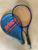 Prince purple tennis racket and blue cover displayed on flat surface