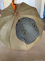Open umbrella showing dinosaur face graphic and orange accents