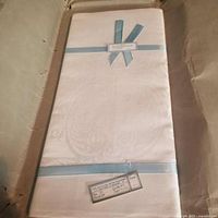 Folded white damask Irish linen tablecloth with blue ribbon inside original wrapping