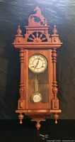 Full front view of walnut regulator wall clock with horse carving and key