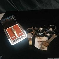 Group shot showing all seven wristwatches on table including Bulova in stand