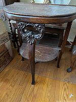Front view of carved solid wood two-tier Victorian side table showing oval top, carved apron, lower shelf and cabriole legs