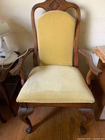 Front view of Queen Anne armchair showing carved crest, arms, yellow upholstery, cabriole legs