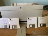 Front view of Apple StyleWriter II printer with four Apple 3.5-inch printer software floppy disks arranged in front