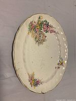 Front view of oval platter showing floral cottage design, scalloped gold rim, staining and chip