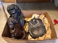 Overall view of three statues in box: two classical male busts and one sleeping cat sculpture