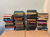 Four stacks of approximately 60 mixed hardcover and paperback books on history, science and reference topics showing spines and wear