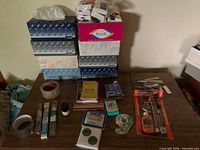 All items displayed on tabletop: stacked tissue boxes, tapes, notebooks, tools, small accessories